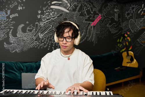 Bild auf Leinwand Young Asian man creates music in a vibrant recording studio filled with creative