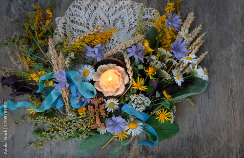 фотографія Herbs, flowers tied to sacred bouquet, cross and candle on table close up