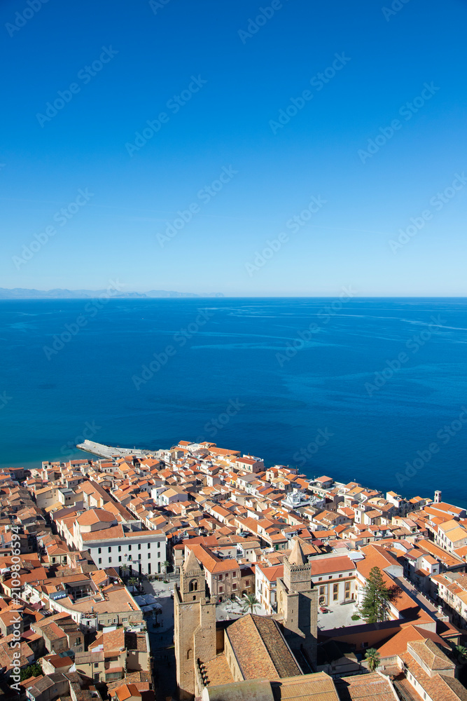 Fototapeta premium Aerial view of the coastal town of Cefalu in Sicily, Italy, showcasing its dense urban landscape and the vast Mediterranean Sea