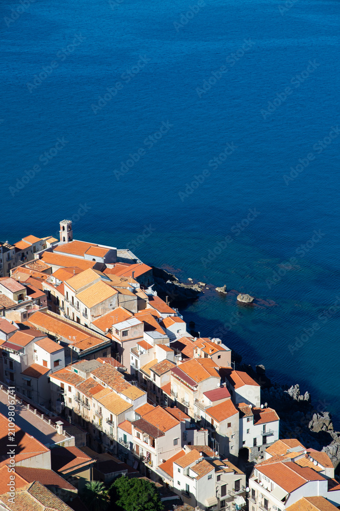 Fototapeta premium Aerial view of the coastal town of Cefalu in Sicily, Italy, showcasing its dense urban landscape and the vast Mediterranean Sea