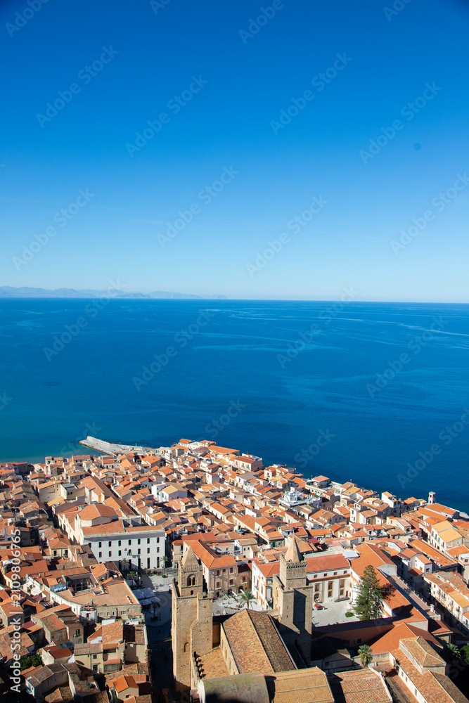Fototapeta premium Aerial view of the coastal town of Cefalu in Sicily, Italy, showcasing its dense urban landscape and the vast Mediterranean Sea