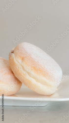 Fotografie Sweet Delights: Two fluffy doughnuts dusted with powdered sugar sit invitingly on a white plate, ready to be savored