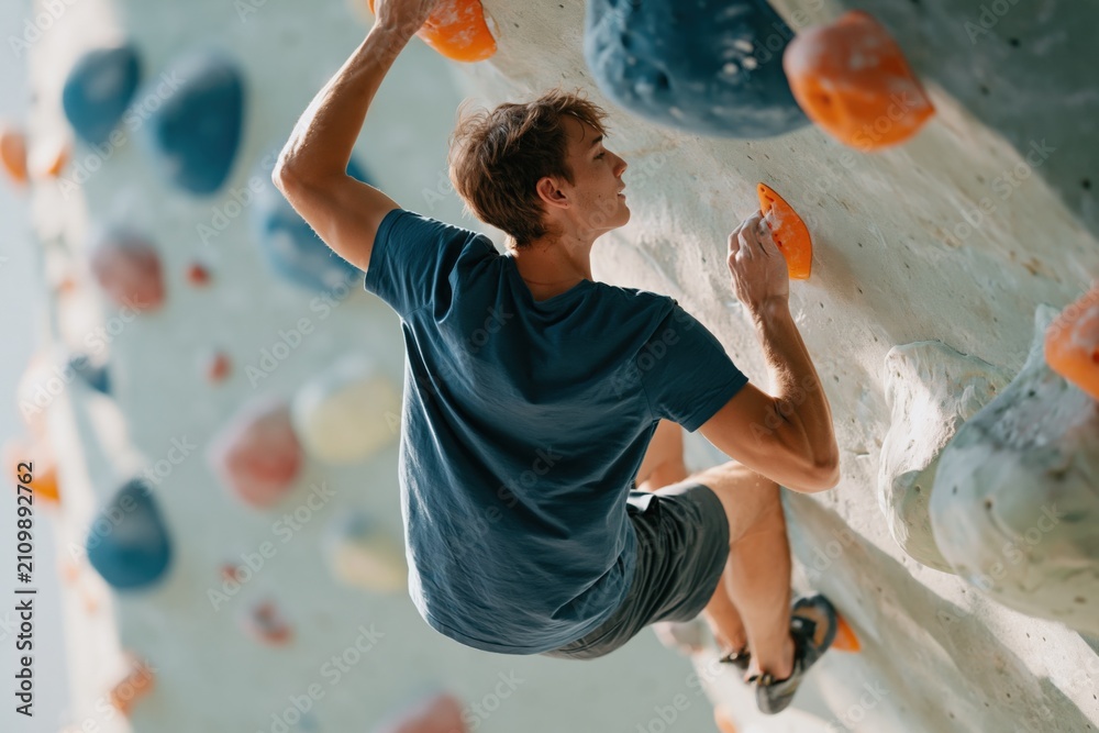 Fototapeta premium Young man indoor bouldering on a climbing wall for fitness poster background and sport training banner