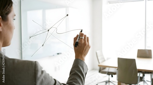 Businesswoman drawing abstract network chart on glass board in office