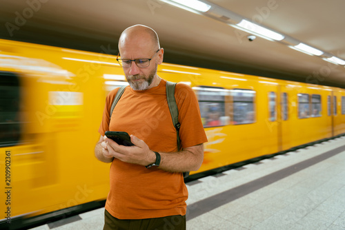 Person using smartphone on subway platform near yellow train