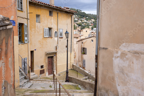 Stone steps wind down through the old town of Grasse, framed by pastel facades and a vintage street lamp.
