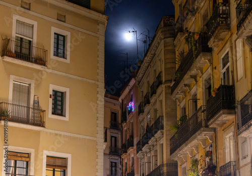 bright full moon shines above the ochre facades and iron balconies of a quiet residential street in the old town