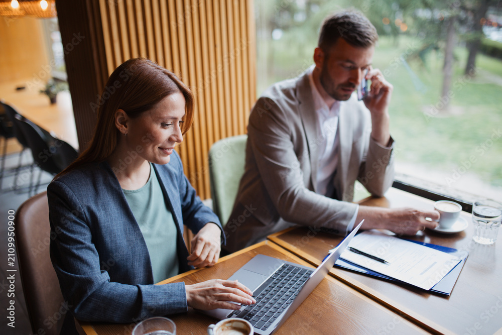 Fototapeta premium Businessman and businesswoman collaborating on a financial report and analyzing data in a coffee shop