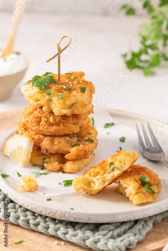 A stack of golden cod fritters on a textured plate with fresh parsley, lemon, and a fork, offering a savory Mediterranean-style seafood appetizer snack