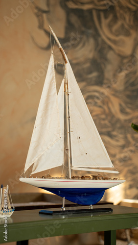 Foto Model Sailboat Decoration: A meticulously crafted model sailboat with white sails and a blue hull stands as an elegant decorative piece, evoking a sense of maritime adventure and classic design