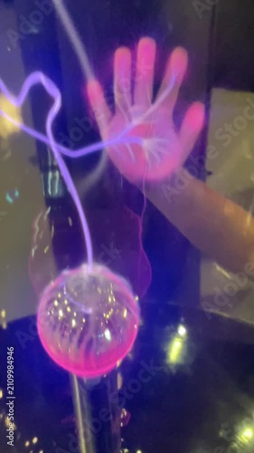 Closeup of transparent plasma ball. Scientific principles in a dark environment. Vertical glowing plasma filaments create a dynamic visual effect. Hand touch 