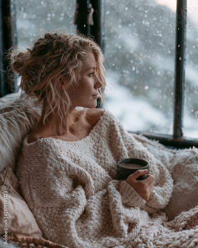 Cozy woman enjoying coffee by window in winter setting.