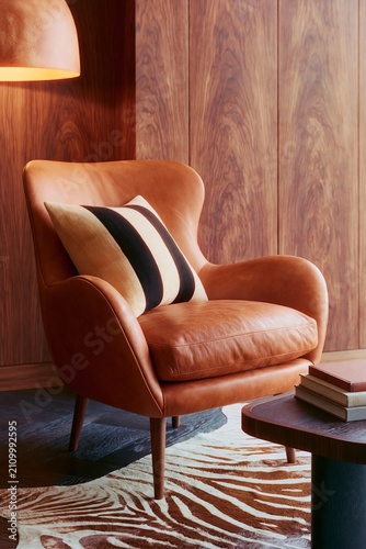 Modern living room corner featuring a warm patinated walnut panel, stylish leather armchair with striped cushion, and decorative coffee table with books