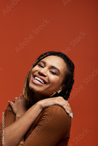 Fotografie A joyful African American woman models her stylish attire in a vibrant orange setting