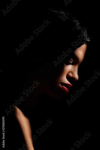 A young beautiful woman showcases her stylish attire while elegantly posing in soft lighting.