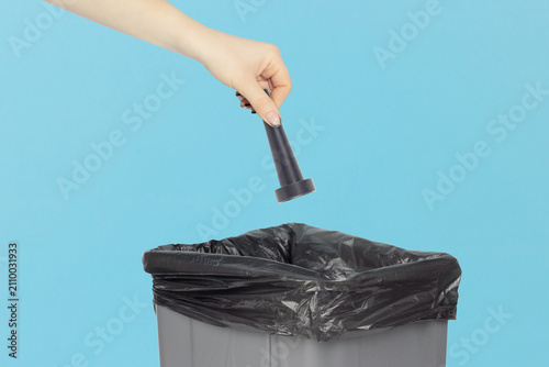 Throwing a long narrow nozzle attachment for electric air duster into the trash can, holding a long narrow nozzle attachment for electric air duster in hand front of the trash can
