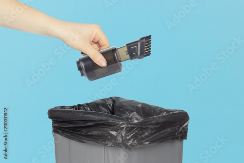 Throwing a dust collector cup with brush nozzle attachment for mini vacuum cleaner into the trash can, holding a dust collection container in hand front of the trash can