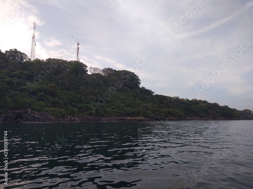Fotografie Calm sea water with ripples against forested coastline under cloudy sky
