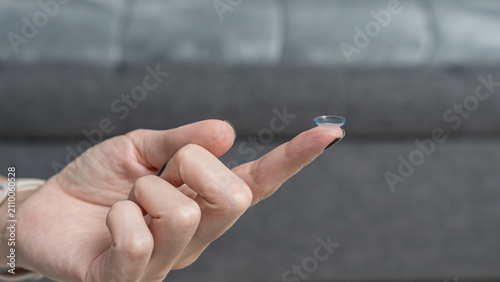 Quadro su tela Teenager holding a single contact lens on their fingertip, with a blurred gray c