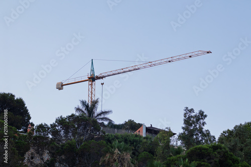 Canvas Print Tower crane extending over green hillside with a clear sky