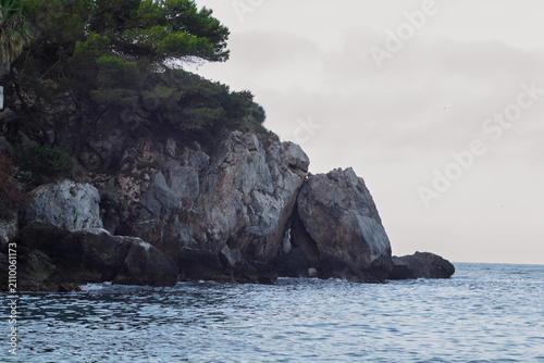 Obraz na płótnie Rocky coastal cliff with green trees and ocean water
