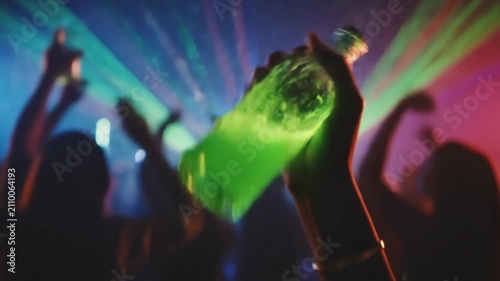Vibrant Nightlife Scene with Glowing Green Drink Bottle Held High in a Crowded Party.