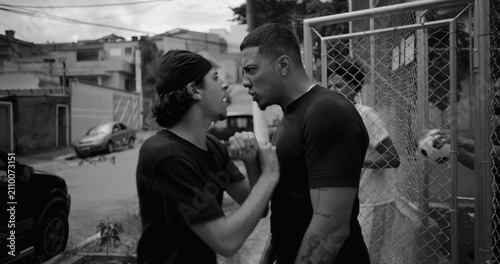 Fotografie Two Hispanic men arguing and pushing each other on street as friends rush in to
