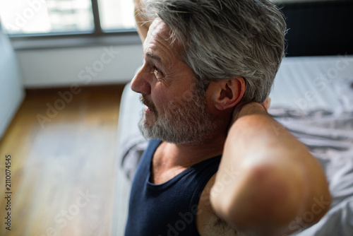 Mature man stretching neck in bedroom