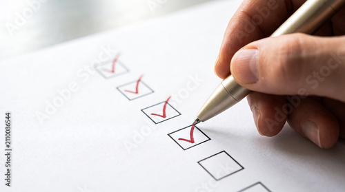 Hand holding metal pen checking items on paper survey list in room.