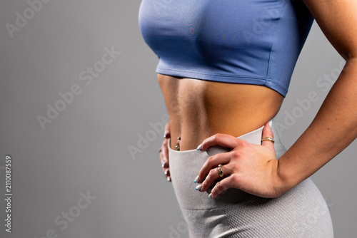 Obraz na plátně Fit woman in blue sports bra and gray leggings showing toned abs with hands on h