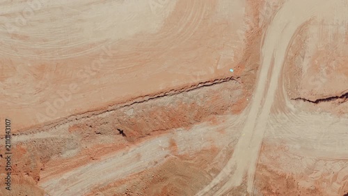 High aerial top-down view flying over a massive construction site, showing heavy machinery, building materials, rebar foundation, and a large tower crane operating on the undeveloped ground