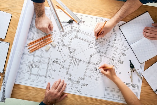Architects reviewing detailed building blueprints on wooden table