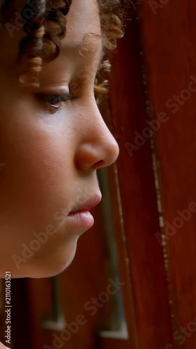 Vertical video: Boy in profile reacting to warm light, blinking and shedding tear at wooden window