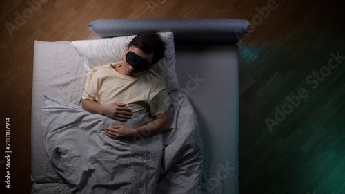 Photography Man sleeping peacefully in bed at night wearing a black eye mask for deep rest a