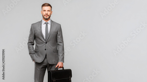 Confident businessman holding briefcase in professional stance. Successful male executive with leather case ready for corporate meeting or financia...