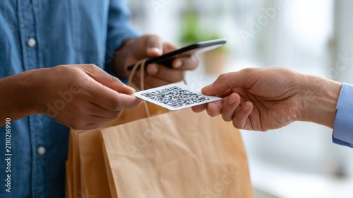 Two individuals exchanging a QR code for contactless payment while holding a paper bag and smartphone in a bright indoor setting with natural light