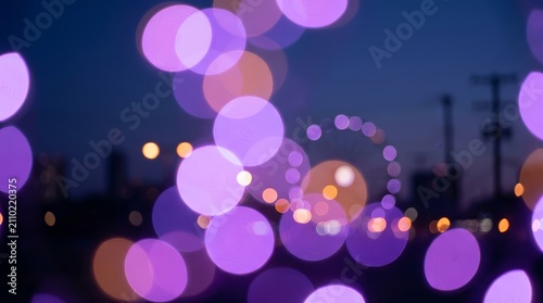 Abstract purple and orange bokeh lights of an amusement park fairground at night.
