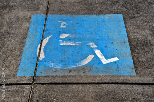 Well worn Faded International Symbol of Access with a stylized image of a person in a wheelchair on blue background 
