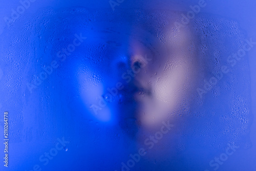 Anonymous black woman portrait behind the wet frost glass in blue light. 
