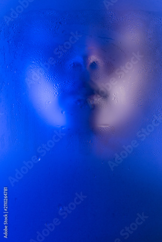 Portrait of young black woman behind wet frosted glass. Closeup of face with closed eyes. Anonymous beauty.