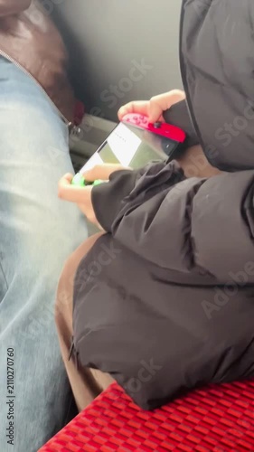 passenger hands holding transit card and phone on red train seat, denim and dark coat visible, quiet travel moment during urban rail journey Video taken on mobile device.