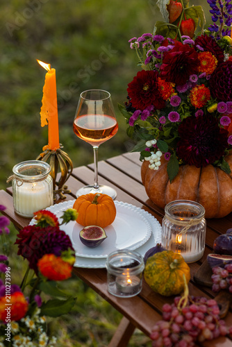 Cozy autumn table decoration for a thanksgiving party outdoors. Grapes, fig, rose wine, candles, pumpkins as decor. Elegant wedding fall arrangement, beautiful setting for a romantic proposal