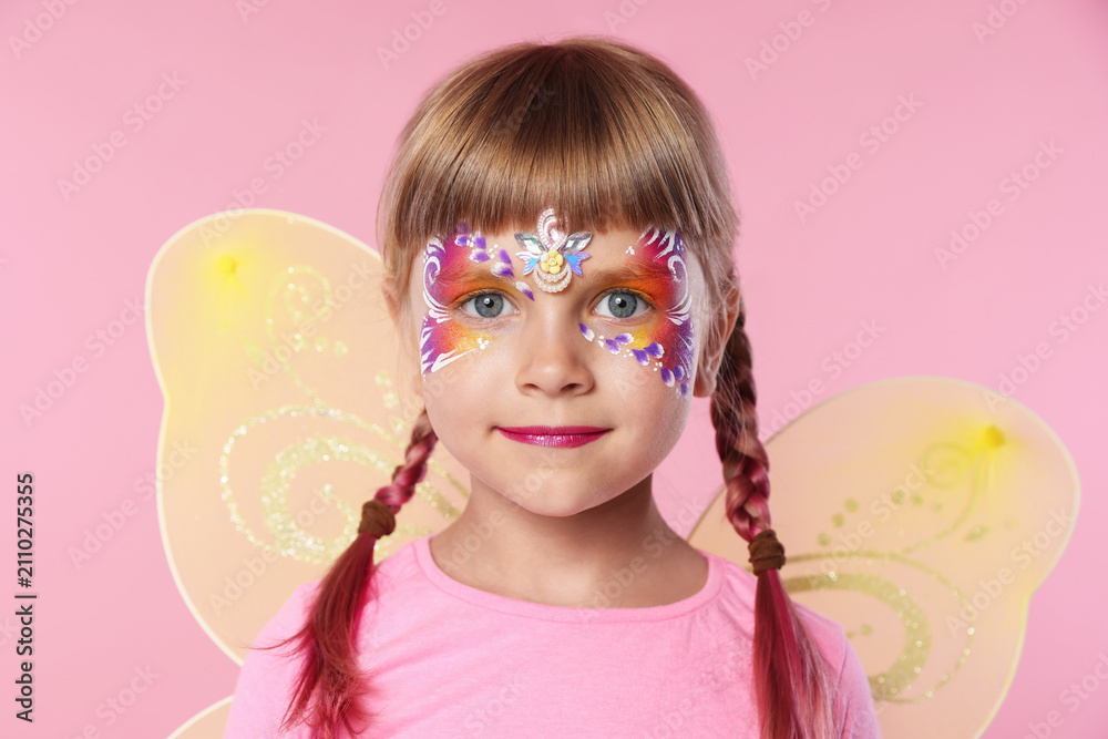 Fototapeta premium Little girl with beautiful face painting and fairy wings on pink background