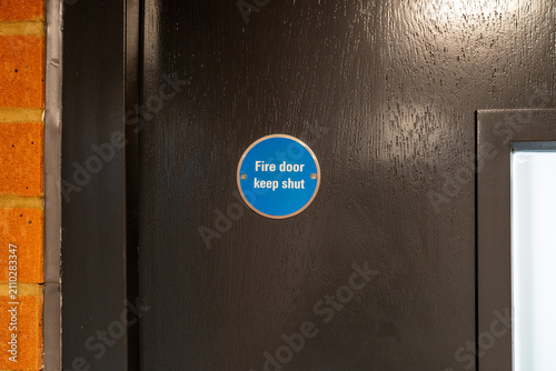 Close-Up of Dark Fire Door With Blue Fire Safety Sign in Indoor Setting