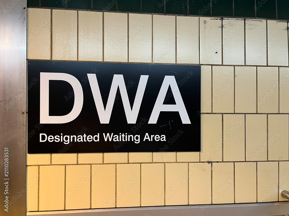 Obraz premium Black DWA Designated Waiting Area sign with white text mounted on yellow subway tile wall in subway transit station, Toronto July 2026