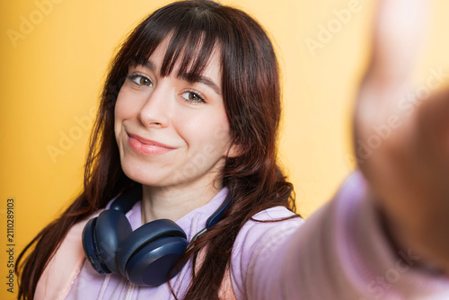 Young woman student sending a friendly selfie gesture while wearing headphones