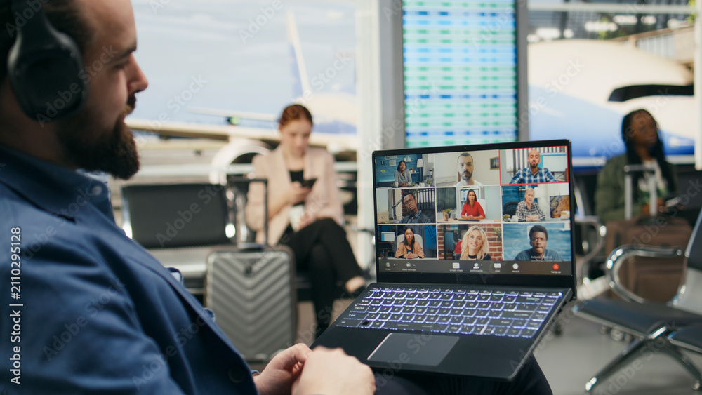 Naklejka premium Businessman attends a laptop video conference in an airport lounge, discussing work with associates and shareholders during business travel and global collaboration.