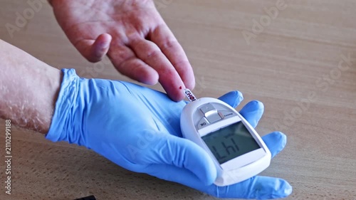 Close up of a medical professional wearing blue gloves using a glucose meter to measure a patient's blood sugar, applying a blood drop from the finger to the test strip