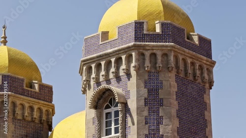 Unique romanticist architectural details of the pena national palace in sintra, portugal, showcasing its famous yellow domes, stone walls, and traditional blue azulejo tiles on a sunny day
