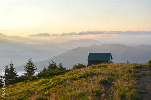 Fotografie Solitary cabin sits on a grassy mountain ridge overlooking a vast, misty valley